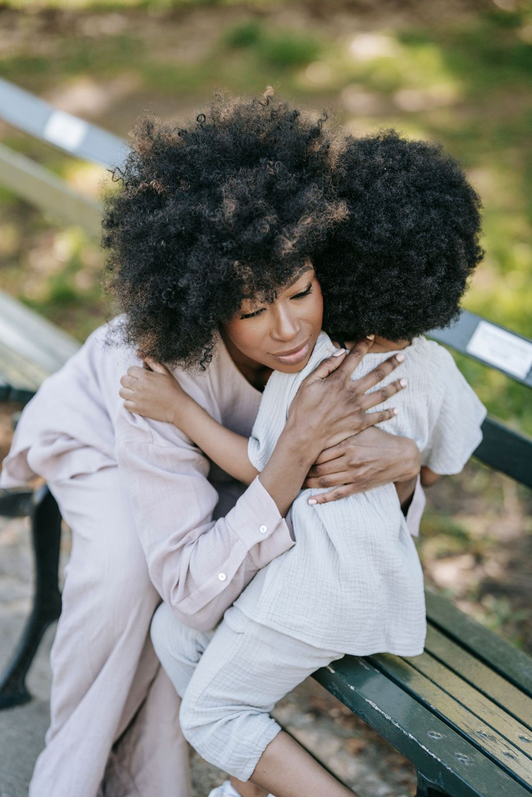 A mum hugging her young child on a park bench