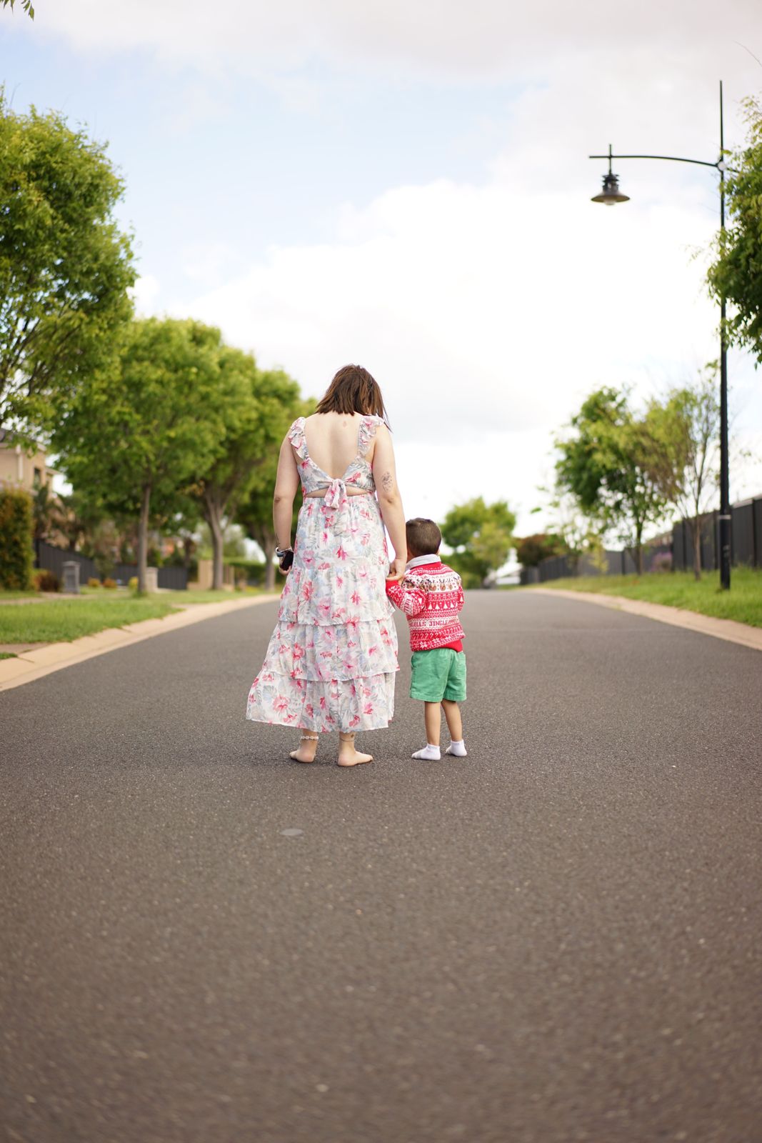 A mum and her young son walking together down a tree lined road